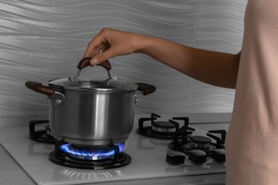 Photo of Woman near gas stove with pot in kitchen, closeup