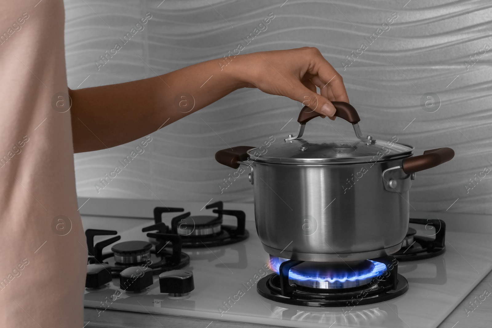 Photo of Woman near gas stove with pot in kitchen, closeup