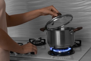 Photo of Woman near gas stove with pot in kitchen, closeup