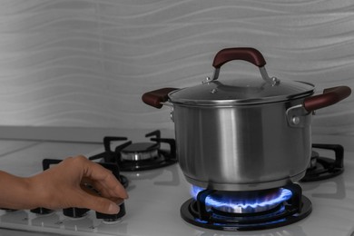 Photo of Woman near gas stove with pot in kitchen, closeup