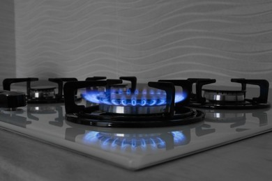 Photo of Modern gas cooktop with burning blue flame in kitchen