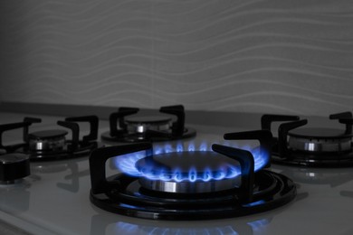 Photo of Modern gas cooktop with burning blue flame in kitchen