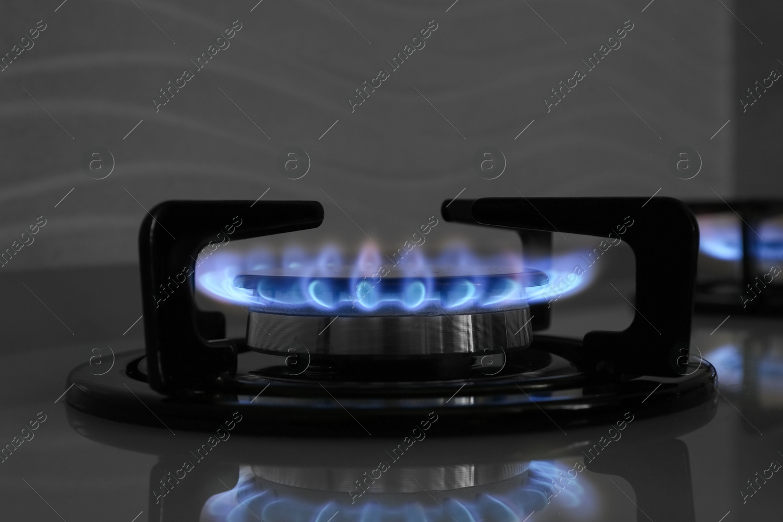 Photo of Gas burner of modern stove with burning blue flame, closeup