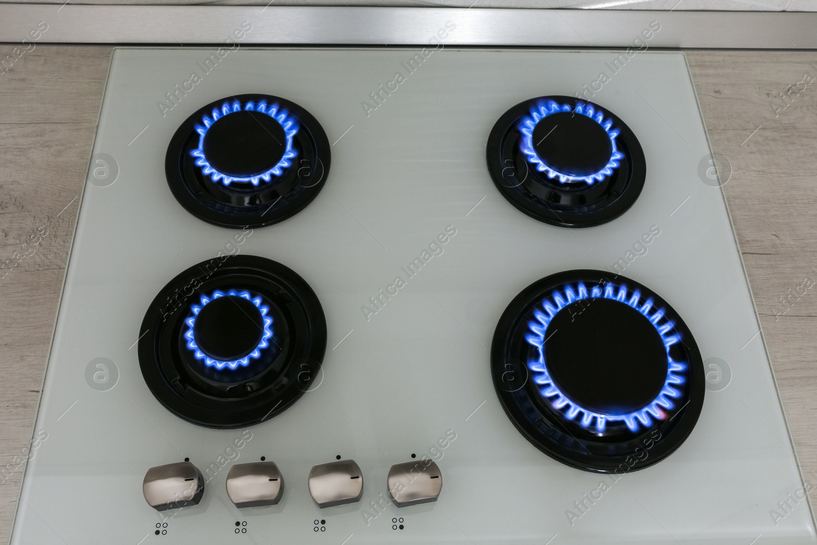 Photo of Modern gas cooktop with burning blue flames in kitchen