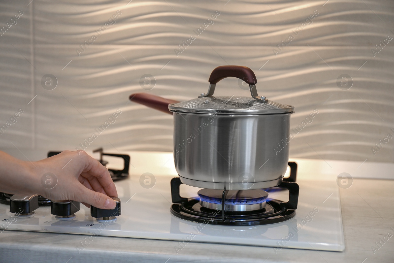 Photo of Woman cooking food in pot on modern kitchen stove with burning gas indoors, closeup