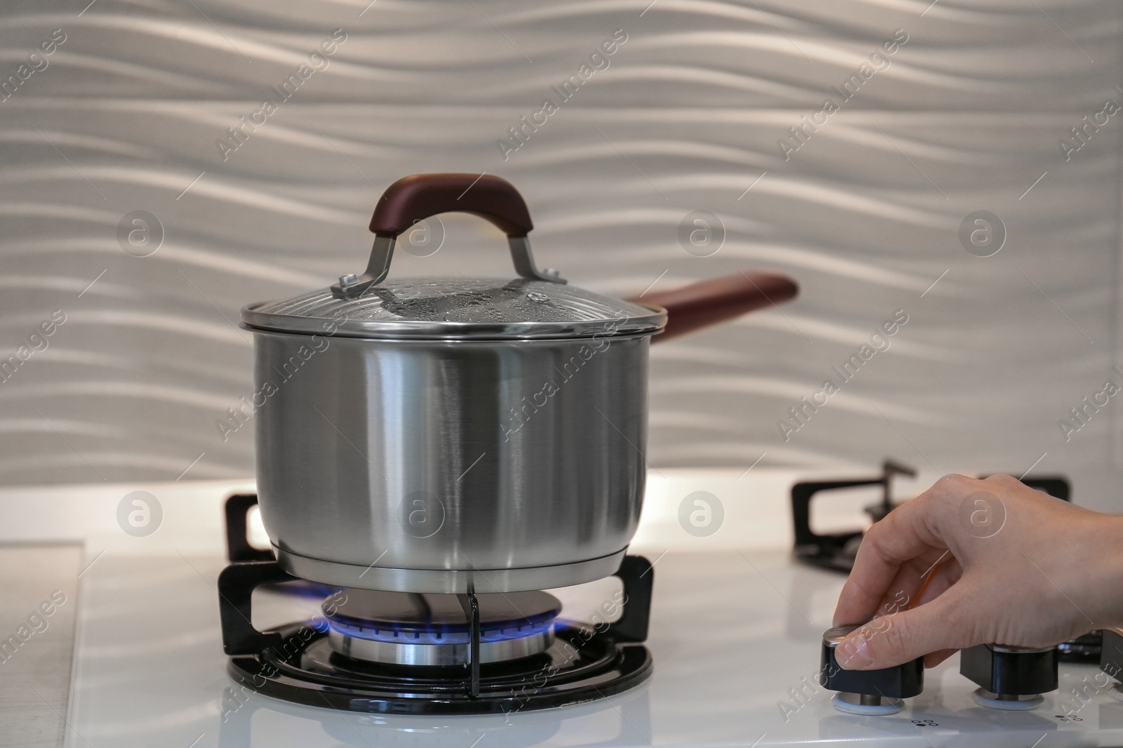 Photo of Woman cooking food in pot on modern kitchen stove with burning gas indoors, closeup