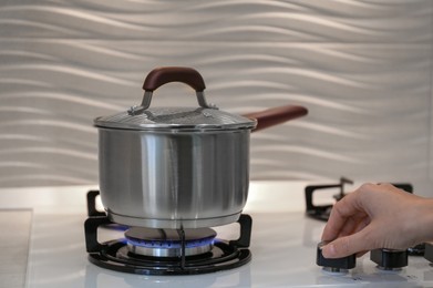 Photo of Woman cooking food in pot on modern kitchen stove with burning gas indoors, closeup