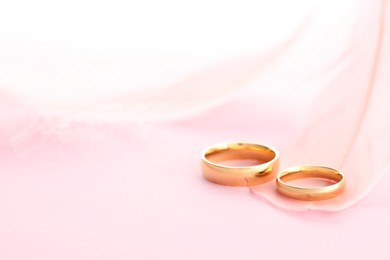 Photo of Beautiful golden wedding rings and feather on pink background, closeup. Space for text