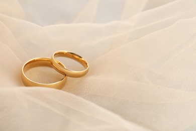 Photo of Beautiful golden wedding rings on beige fabric, space for text