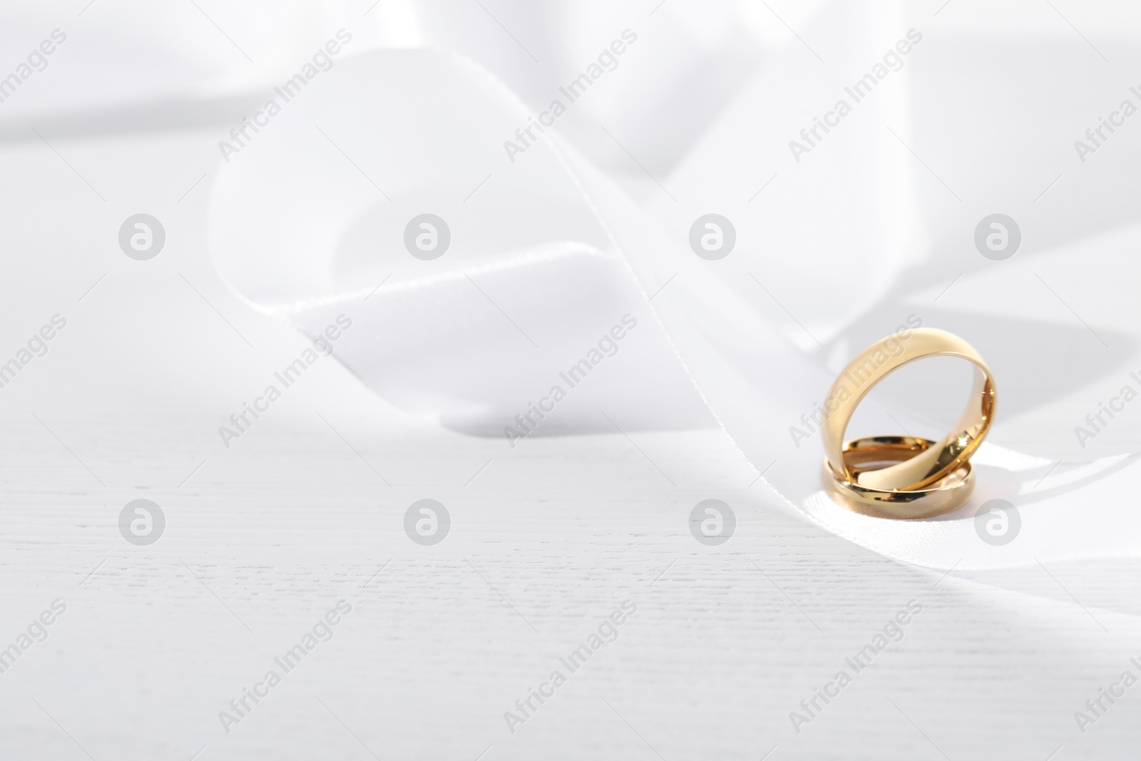 Photo of Beautiful golden wedding rings and white ribbon on light wooden background