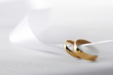 Photo of Beautiful golden wedding rings and white ribbon on light wooden background