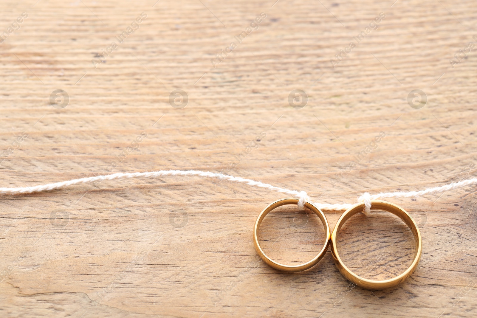 Photo of Beautiful golden wedding rings tied with thread on wooden background, above view. Space for text