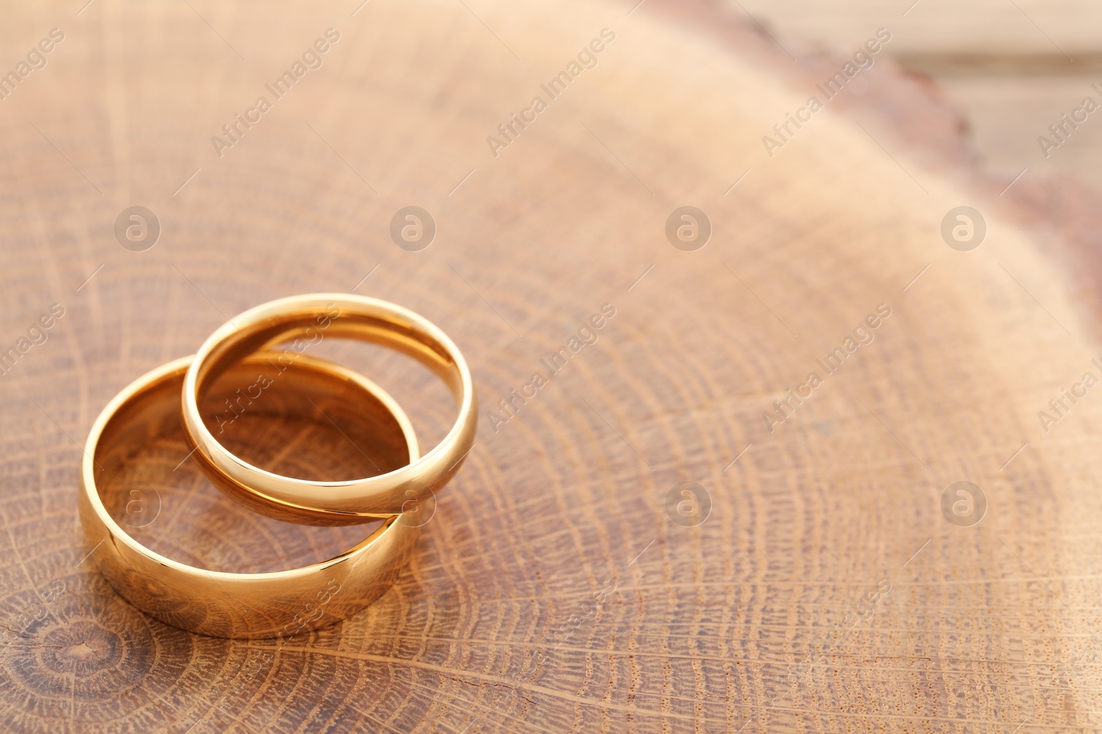 Photo of Beautiful golden wedding rings on wooden background, space for text