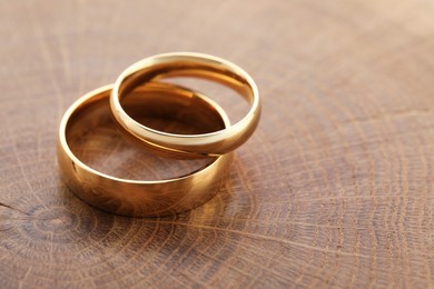 Photo of Beautiful golden wedding rings on wooden background, closeup