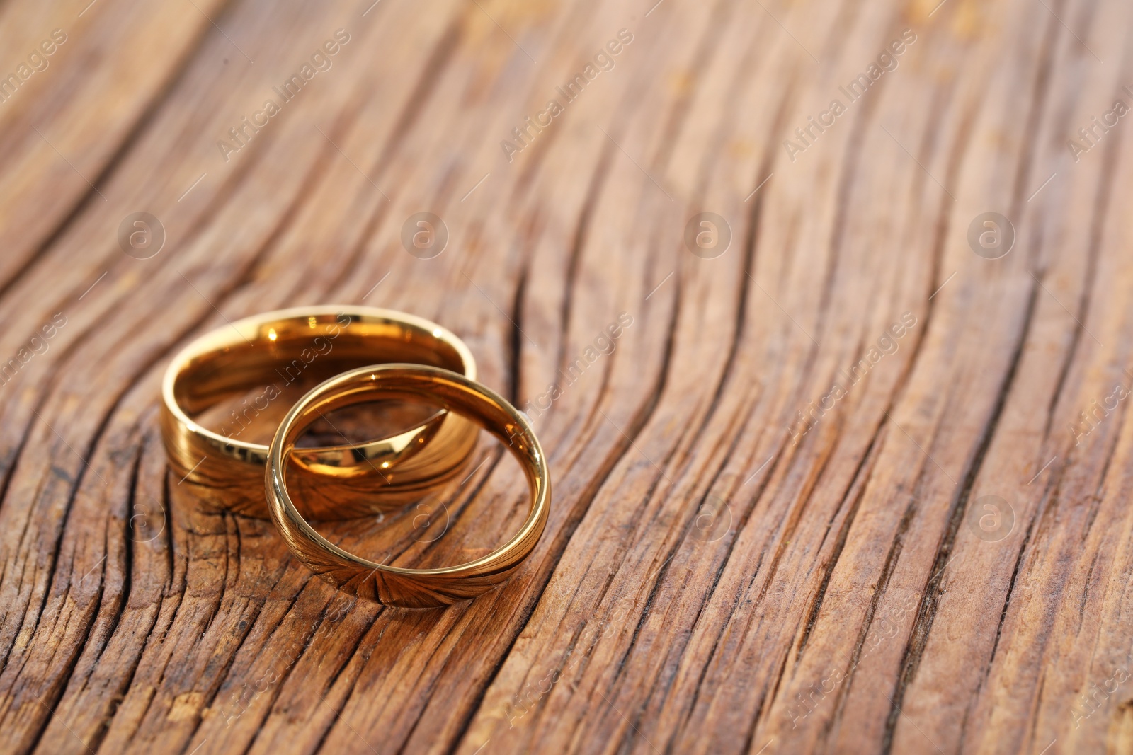 Photo of Beautiful golden wedding rings on wooden background, space for text