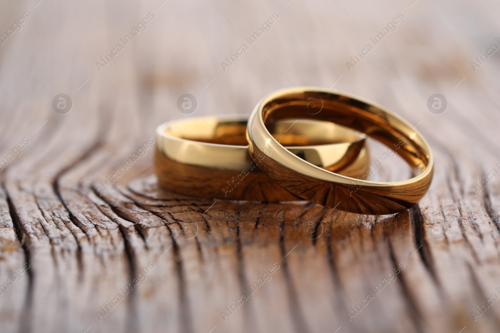 Photo of Beautiful golden wedding rings on wooden background, closeup