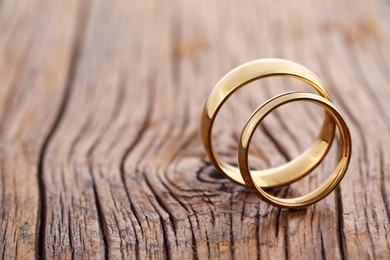 Photo of Beautiful golden wedding rings on wooden background, closeup. Space for text