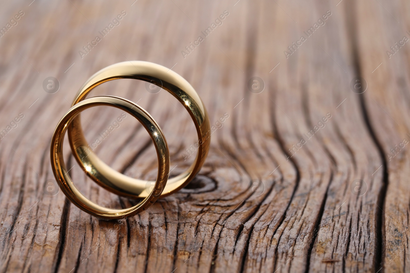 Photo of Beautiful golden wedding rings on wooden background, space for text