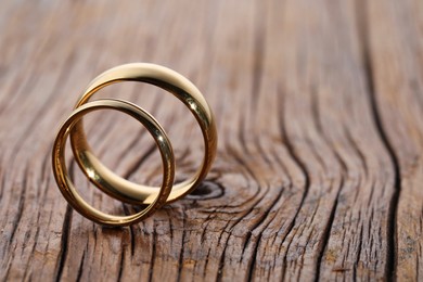 Photo of Beautiful golden wedding rings on wooden background, space for text