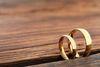 Photo of Beautiful golden wedding rings on wooden background, space for text