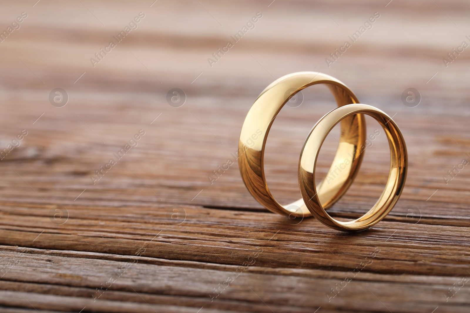 Photo of Beautiful golden wedding rings on wooden background, space for text