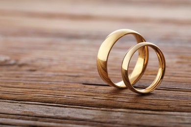 Photo of Beautiful golden wedding rings on wooden background, space for text