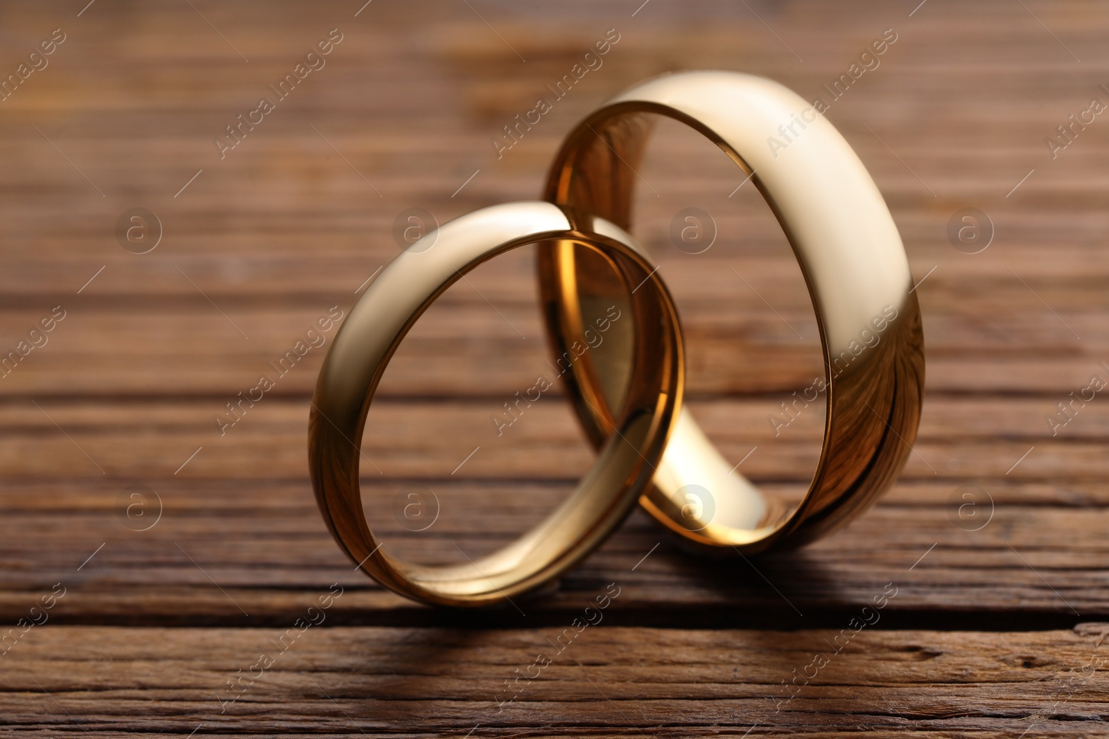 Photo of Beautiful golden wedding rings on wooden background, closeup