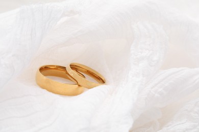 Photo of Beautiful golden wedding rings on white fabric, closeup