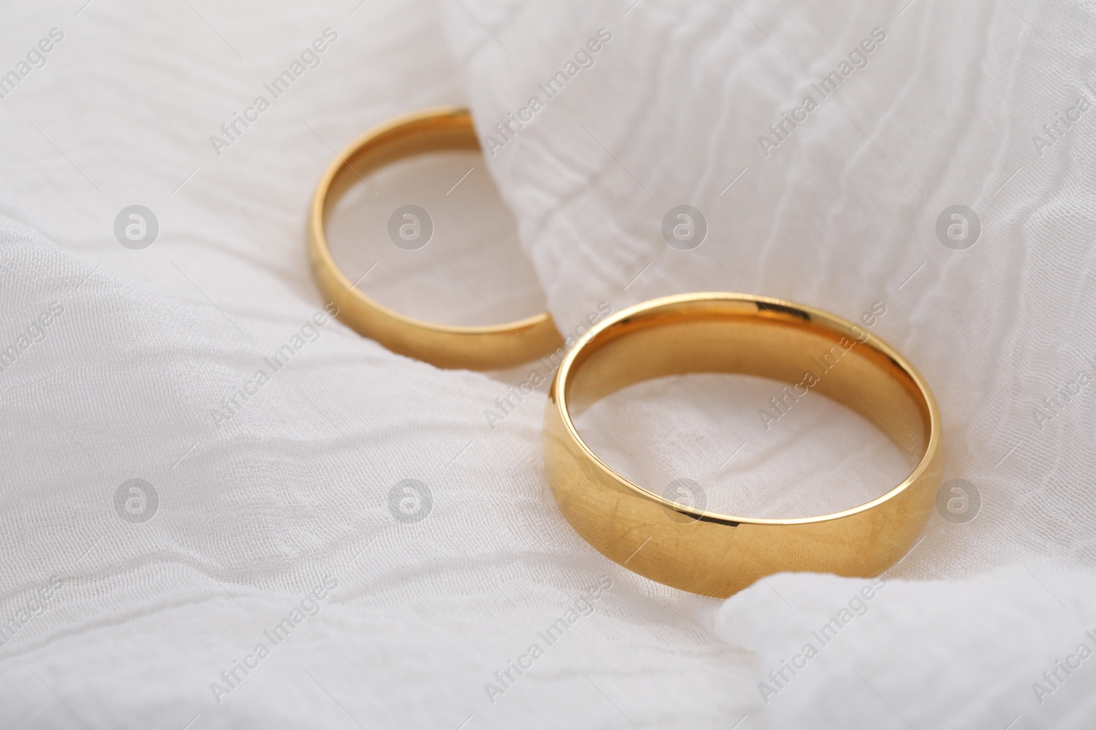 Photo of Beautiful golden wedding rings on white fabric, closeup