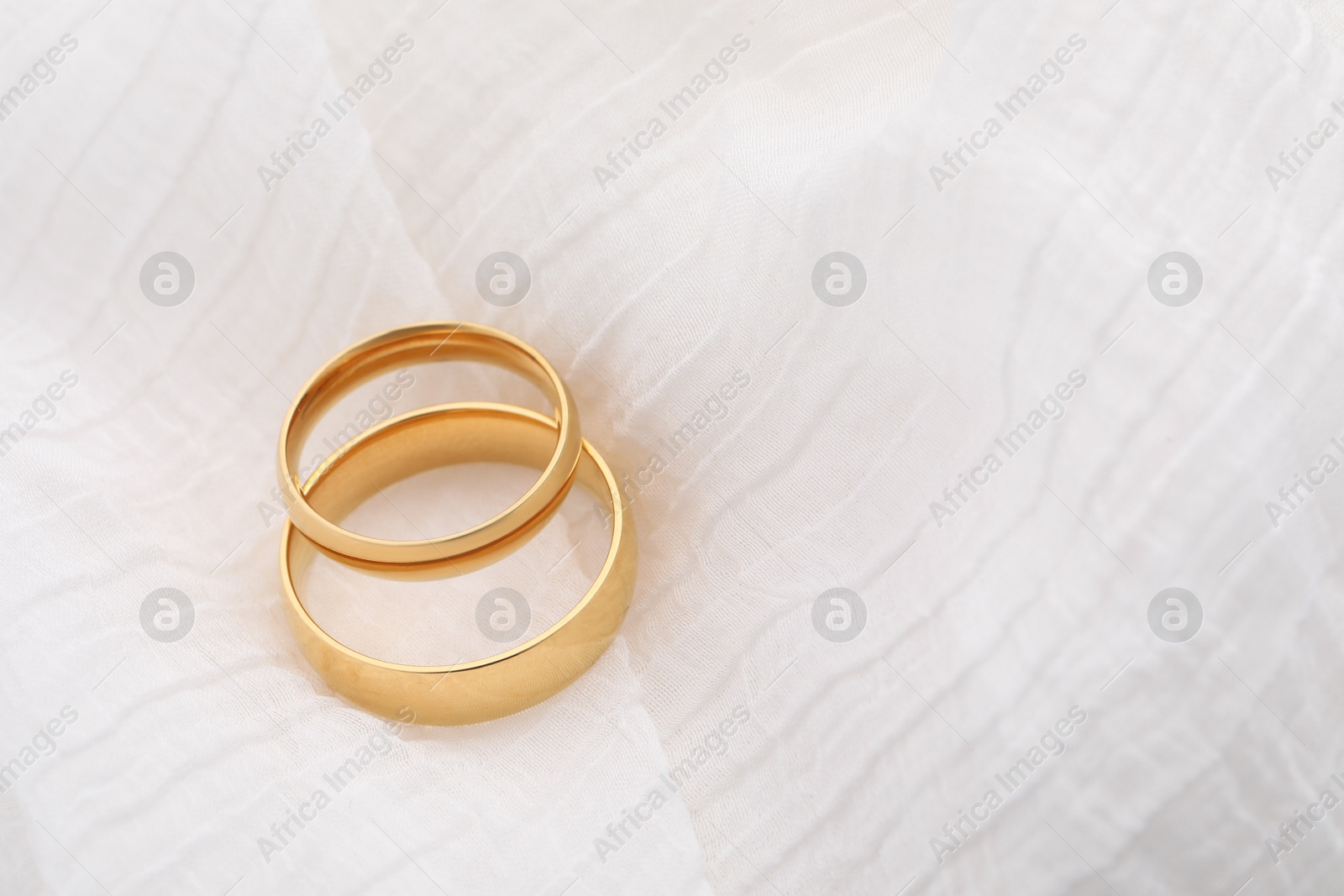 Photo of Beautiful golden wedding rings on white fabric, space for text