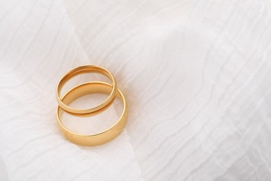 Photo of Beautiful golden wedding rings on white fabric, space for text