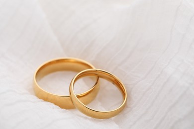 Photo of Beautiful golden wedding rings on white fabric, closeup. Space for text