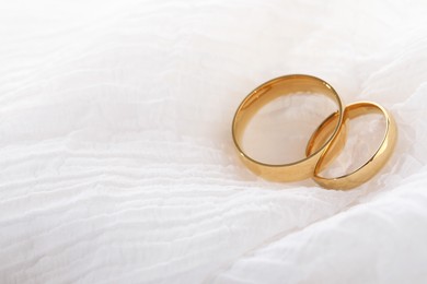 Photo of Beautiful golden wedding rings on white fabric, space for text