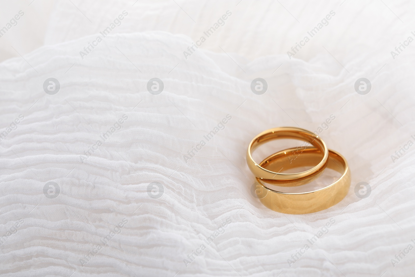 Photo of Beautiful golden wedding rings on white fabric, space for text