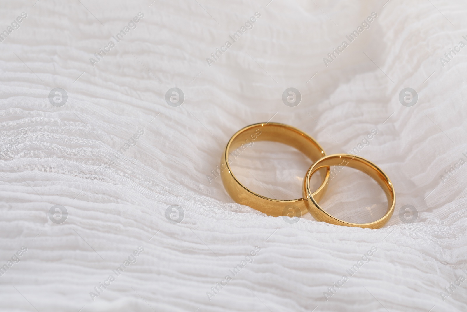 Photo of Beautiful golden wedding rings on white fabric, space for text