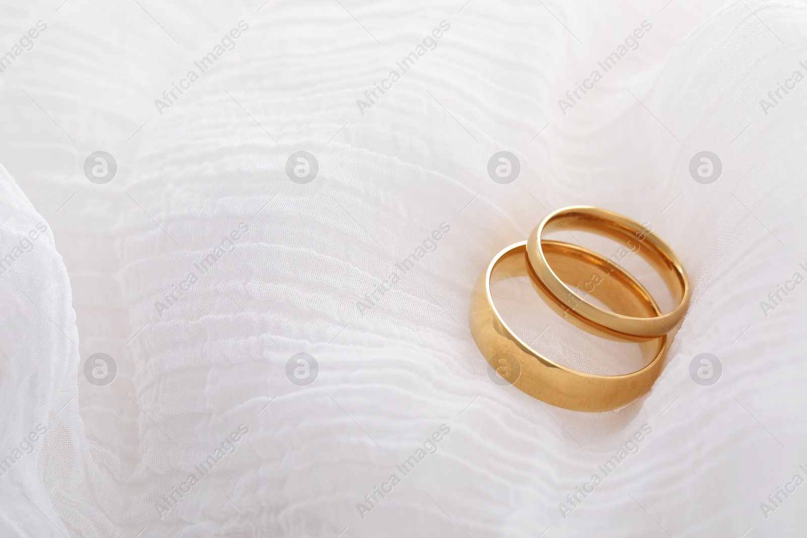 Photo of Beautiful golden wedding rings on white fabric, space for text