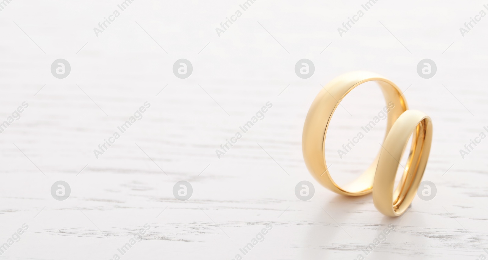 Photo of Beautiful golden wedding rings on light wooden background, space for text