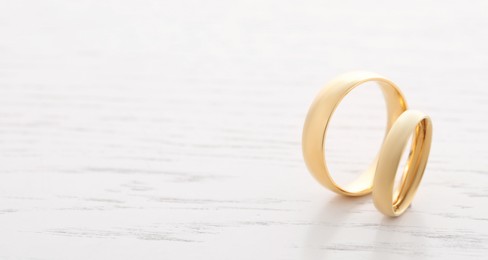 Photo of Beautiful golden wedding rings on light wooden background, space for text