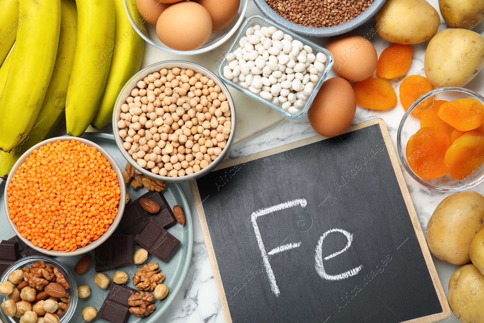 Photo of Different products rich in iron and small chalkboard with Ferrum symbol on white marble table, flat lay. Diet plan for anemia