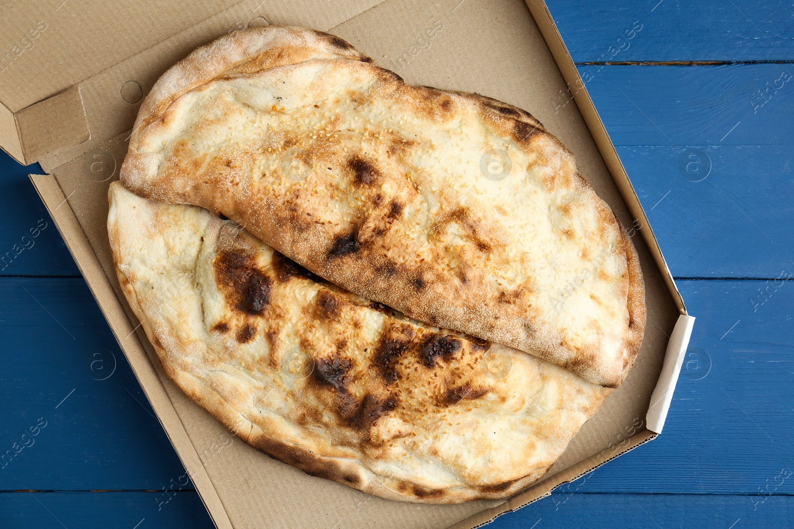 Photo of Tasty calzones in cardboard box on blue wooden table, top view