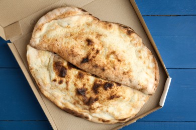 Photo of Tasty calzones in cardboard box on blue wooden table, top view