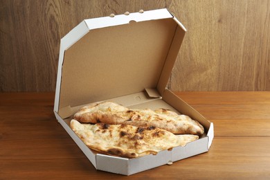 Photo of Tasty calzones in cardboard box on wooden table, closeup