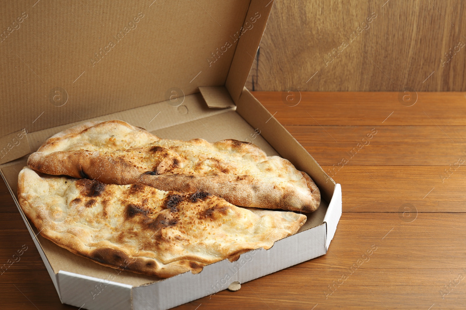 Photo of Tasty calzones in cardboard box on wooden table, closeup. Space for text