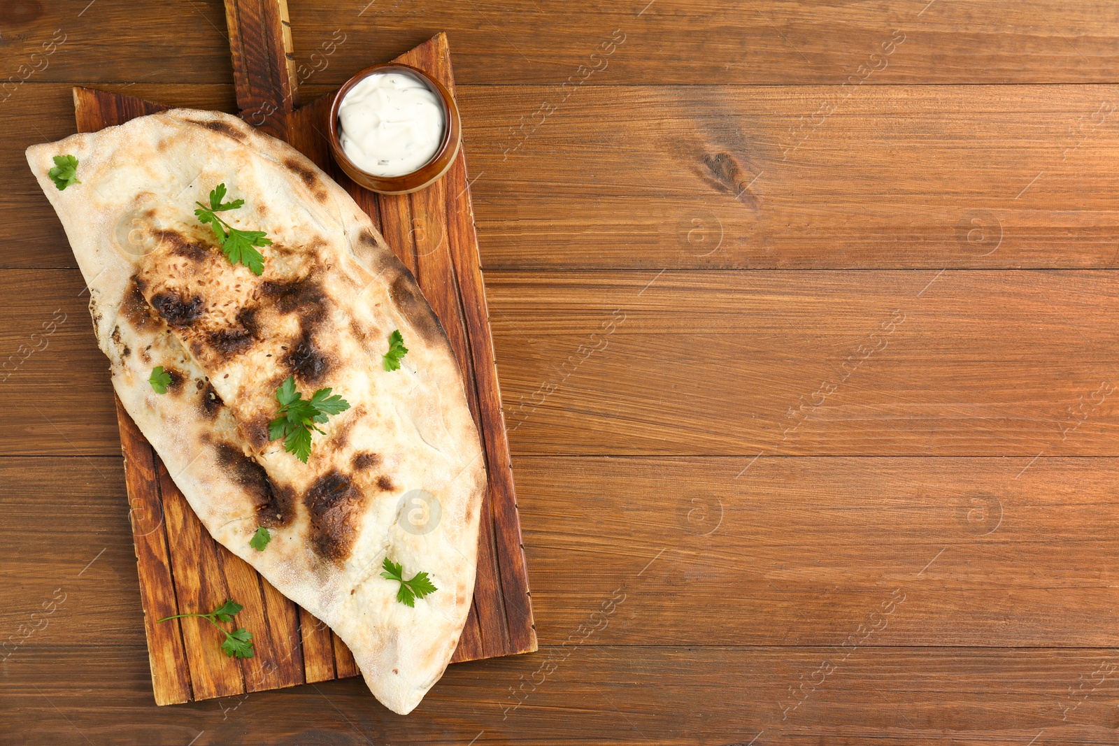 Photo of Board with tasty calzone, parsley and sauce on wooden table, top view. Space for text