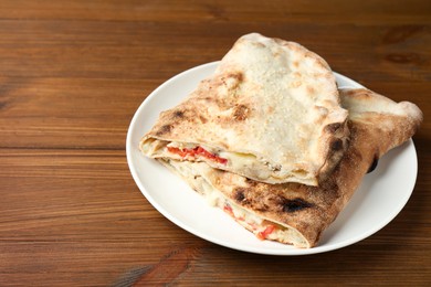 Photo of Halves of tasty calzone with meat, cheese and tomato on wooden table, closeup. Space for text