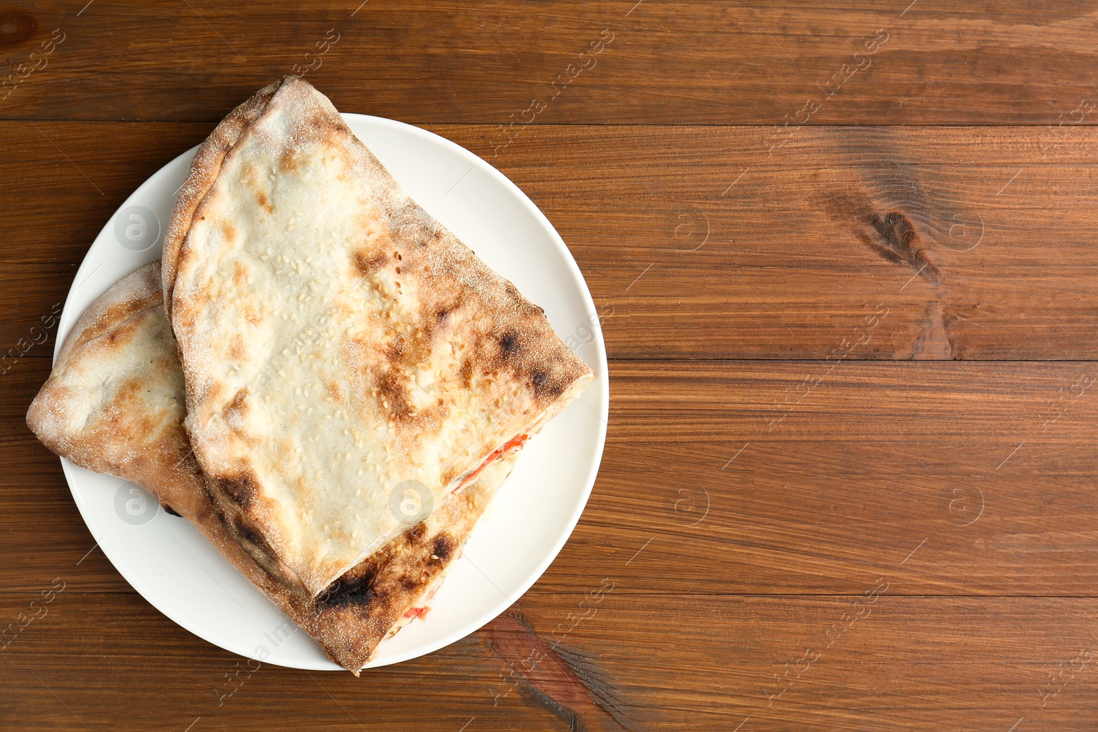 Photo of Halves of tasty calzone on wooden table, top view. Space for text