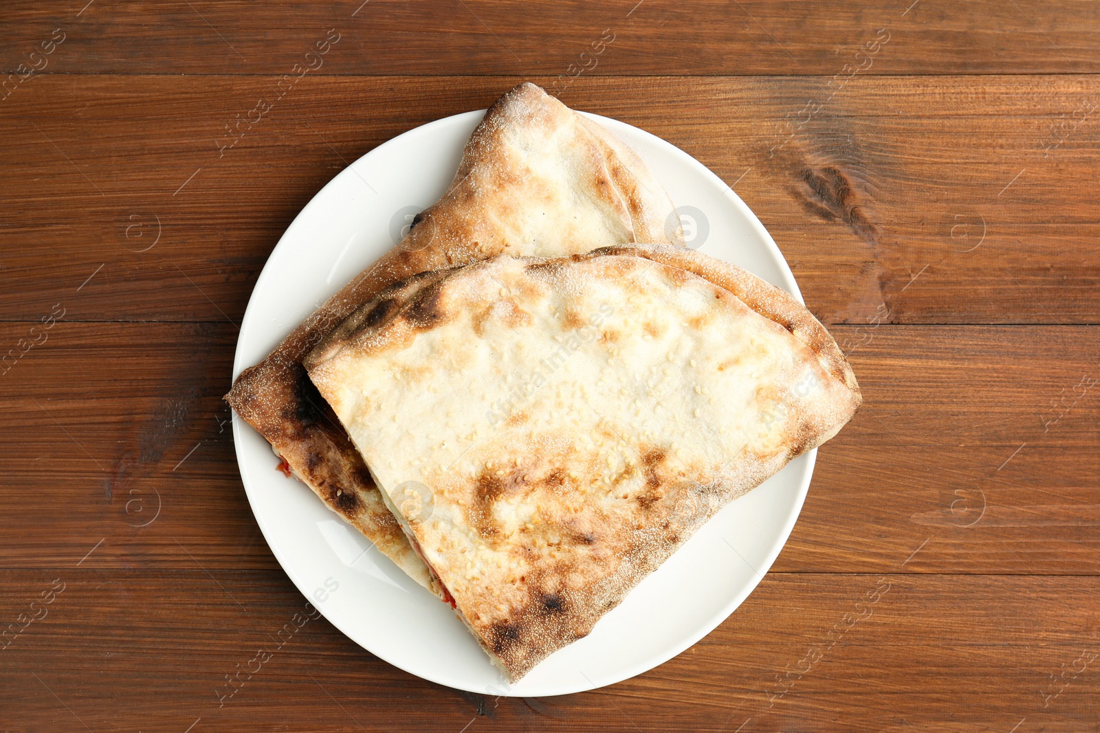 Photo of Halves of tasty calzone on wooden table, top view