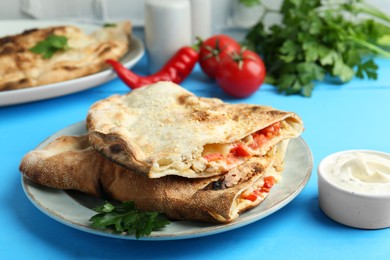 Photo of Halves of tasty calzone with meat, cheese, tomato and sauce on light blue table, closeup