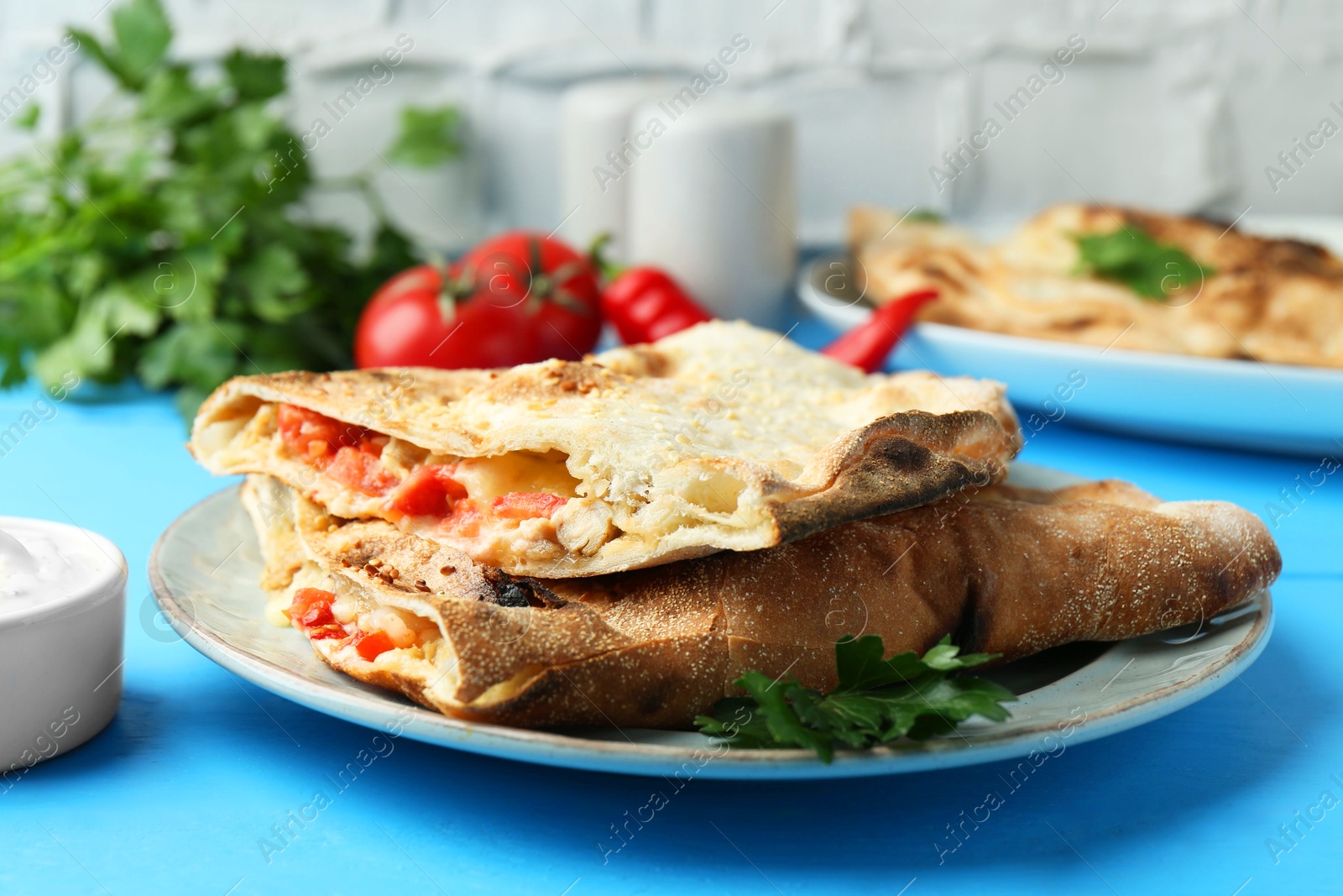 Photo of Halves of tasty calzone with meat, cheese, tomato and sauce on light blue table, closeup