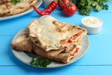 Photo of Halves of tasty calzone with meat, cheese, tomato and sauce on light blue table, closeup